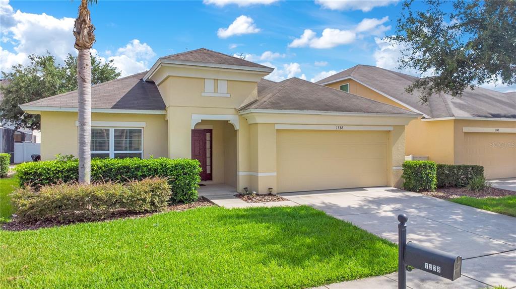 A single-story house with a tan stucco exterior, a two-car garage, and a front lawn — 1338 YORKSHIRE COURT, DAVENPORT, FL