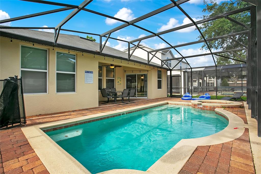 A swimming pool with a spa is enclosed by a screened lanai behind a house — 1338 YORKSHIRE COURT, DAVENPORT, FL