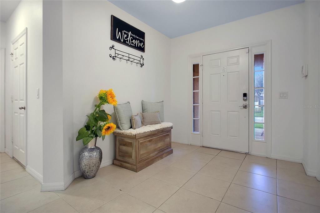 An entryway features a wooden storage bench, a sunflower vase, and a white front door — 1338 YORKSHIRE COURT, DAVENPORT, FL