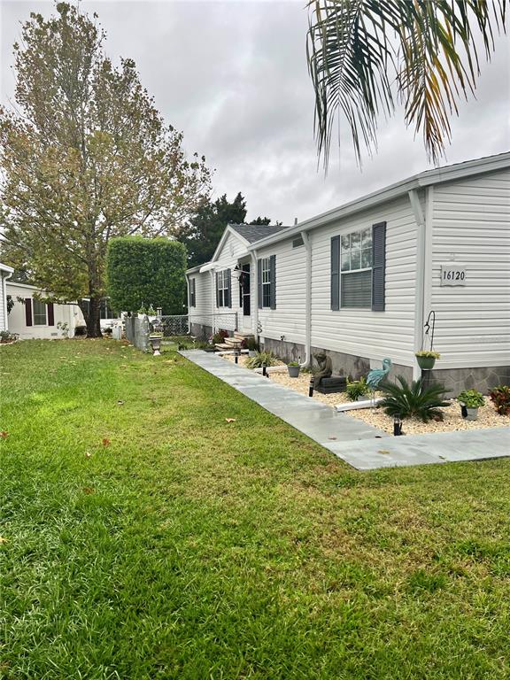 The exterior of a light-colored manufactured home features a concrete walkway and a large tree — 16120 BROOKRIDGE BOULEVARD, BROOKSVILLE, FL