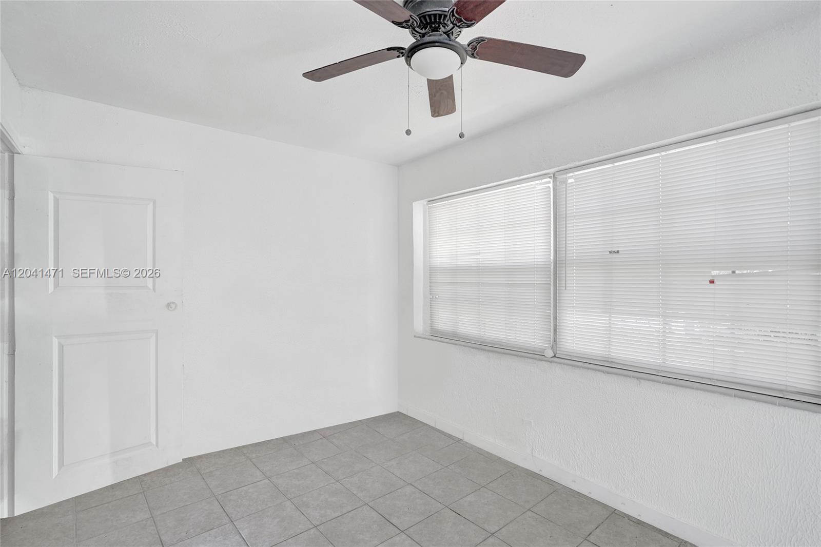 A small, empty room features white walls, gray tile flooring, a ceiling fan, and windows — 701 SW 7th St, Pompano Beach FL 33060, POMPANO BEACH, FL