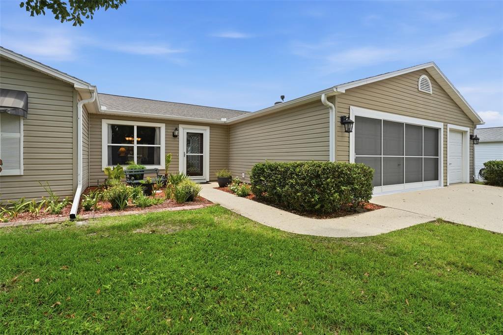 A tan-sided house features a front entrance, a garage with a screen door, and landscaping — 1602 MALACARA LANE, THE VILLAGES, FL