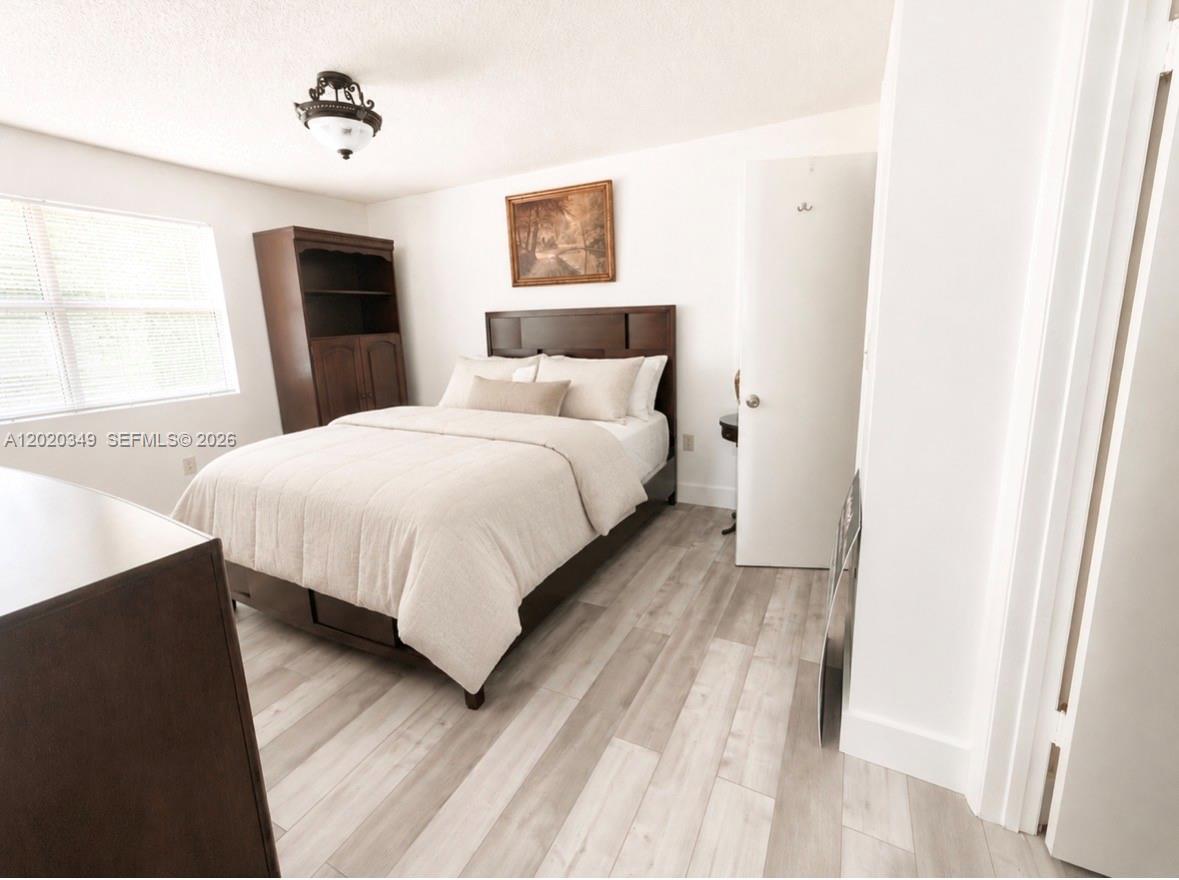 A bedroom features a dark wood bed frame, light wood-look flooring, and a white door — 10440 SW 156th Ct # 726, Miami FL 33196, MIAMI, FL