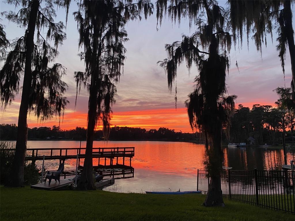 A wooden dock extends into a lake at sunset, framed by trees with hanging moss — 18010 CLEAR LAKE DRIVE, LUTZ, FL