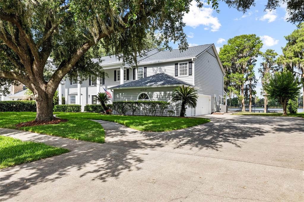 A two-story light gray house with a front lawn, large oak tree, and concrete driveway — 18010 CLEAR LAKE DRIVE, LUTZ, FL