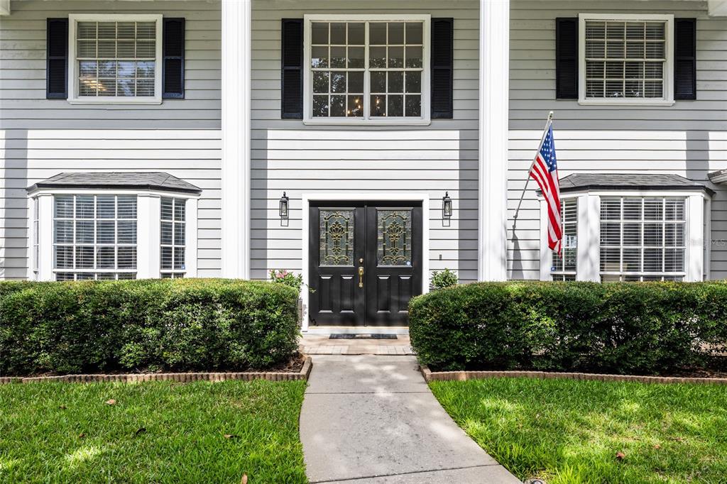 A two-story house exterior features gray siding, a black double front door, and bay windows — 18010 CLEAR LAKE DRIVE, LUTZ, FL