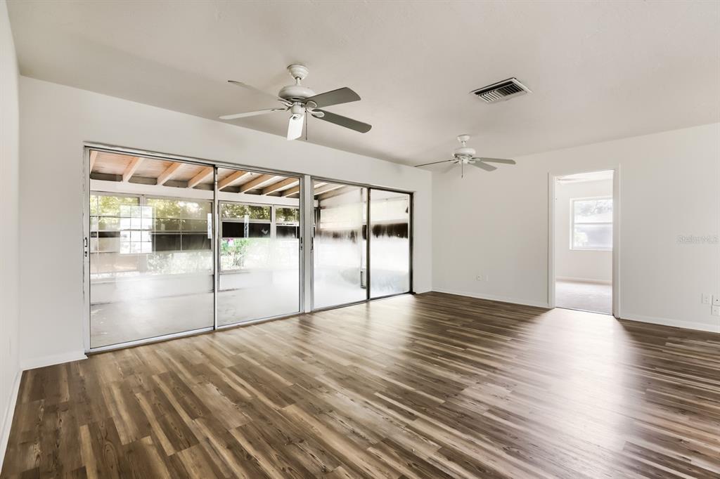 A living room with wood-look flooring, two ceiling fans, and large sliding glass doors — 1252 GARRET AVENUE, SPRING HILL, FL