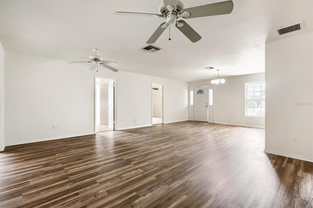 A spacious, empty living room features wood-look flooring, white walls, and two ceiling fans — 1252 GARRET AVENUE, SPRING HILL, FL