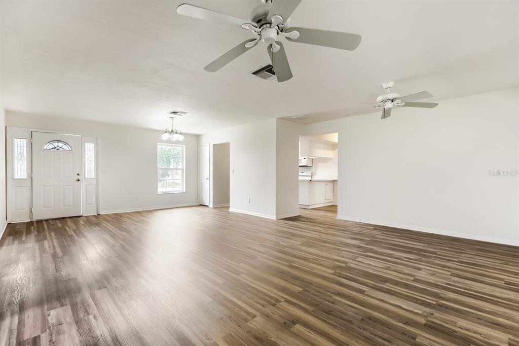 A bright, open-concept living area features light wood-look flooring, white walls, and two ceiling fans — 1252 GARRET AVENUE, SPRING HILL, FL