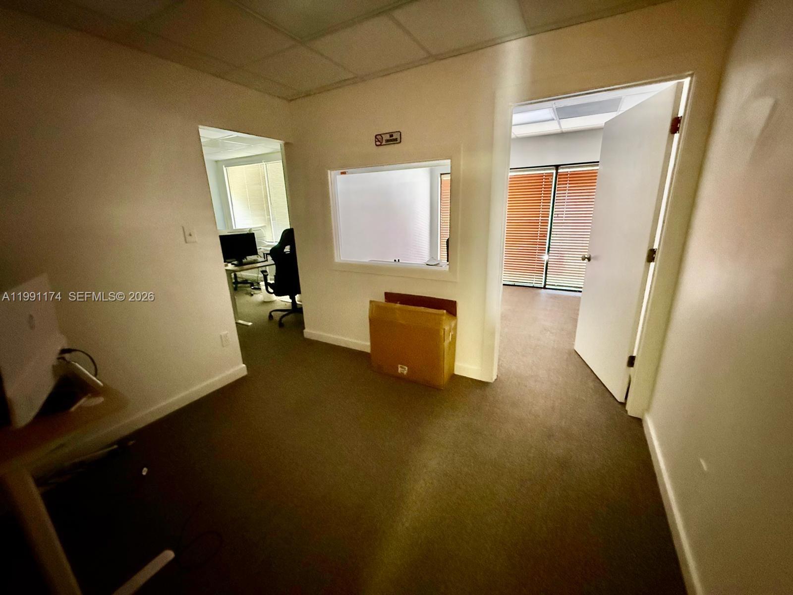 An office space features carpeted floors, a central window, and an open doorway leading to another room — 12016 SW 132nd Ct, Miami FL 33186, MIAMI, FL