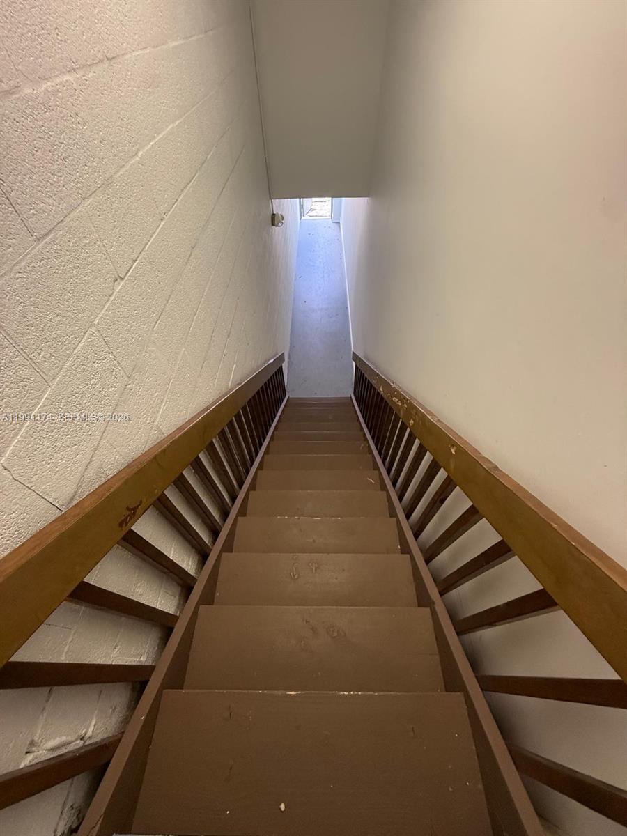 A narrow wooden staircase descends between a white painted brick wall and a wooden railing — 12016 SW 132nd Ct, Miami FL 33186, MIAMI, FL