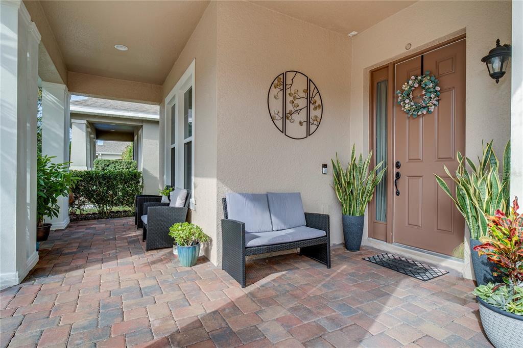 A covered front porch features brick pavers, a brown door with a wreath, and seating — 15755 SWEET LIMETTA DRIVE, WINTER GARDEN, FL