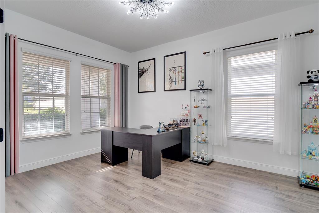 A home office features wood-look flooring, a dark L-shaped desk, and two glass display cabinets — 15755 SWEET LIMETTA DRIVE, WINTER GARDEN, FL