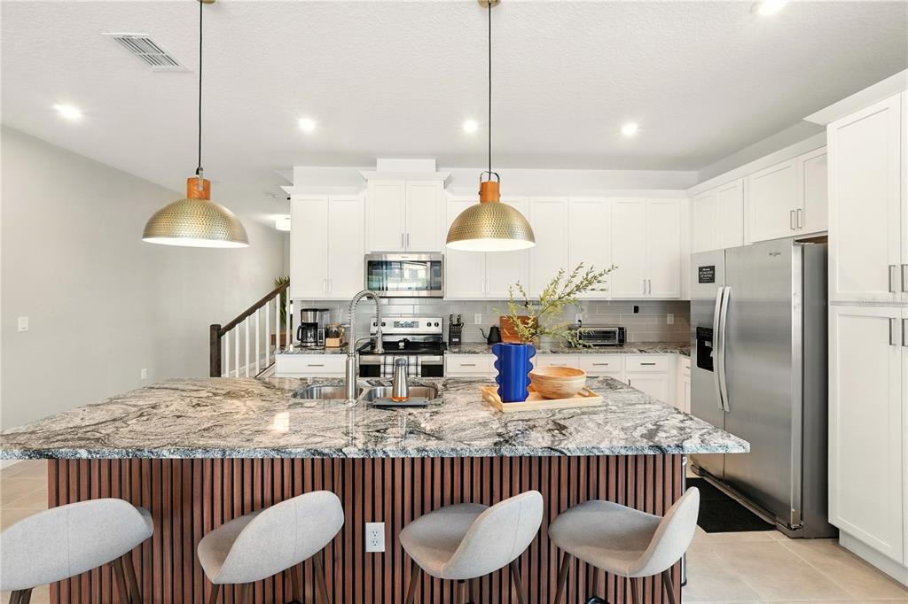 A kitchen features a granite-topped island, white cabinetry, stainless steel appliances, and two pendant lights — 2306 ZABALLINA PLACE, KISSIMMEE, FL
