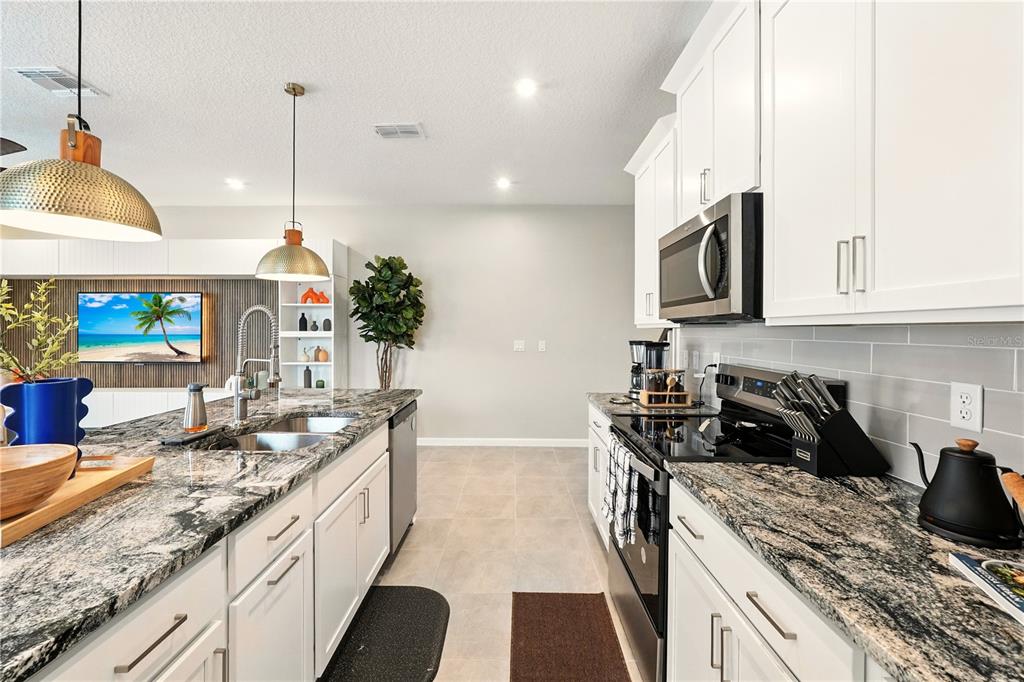 A modern kitchen features white cabinets, granite countertops, stainless steel appliances, and two pendant lights — 2306 ZABALLINA PLACE, KISSIMMEE, FL