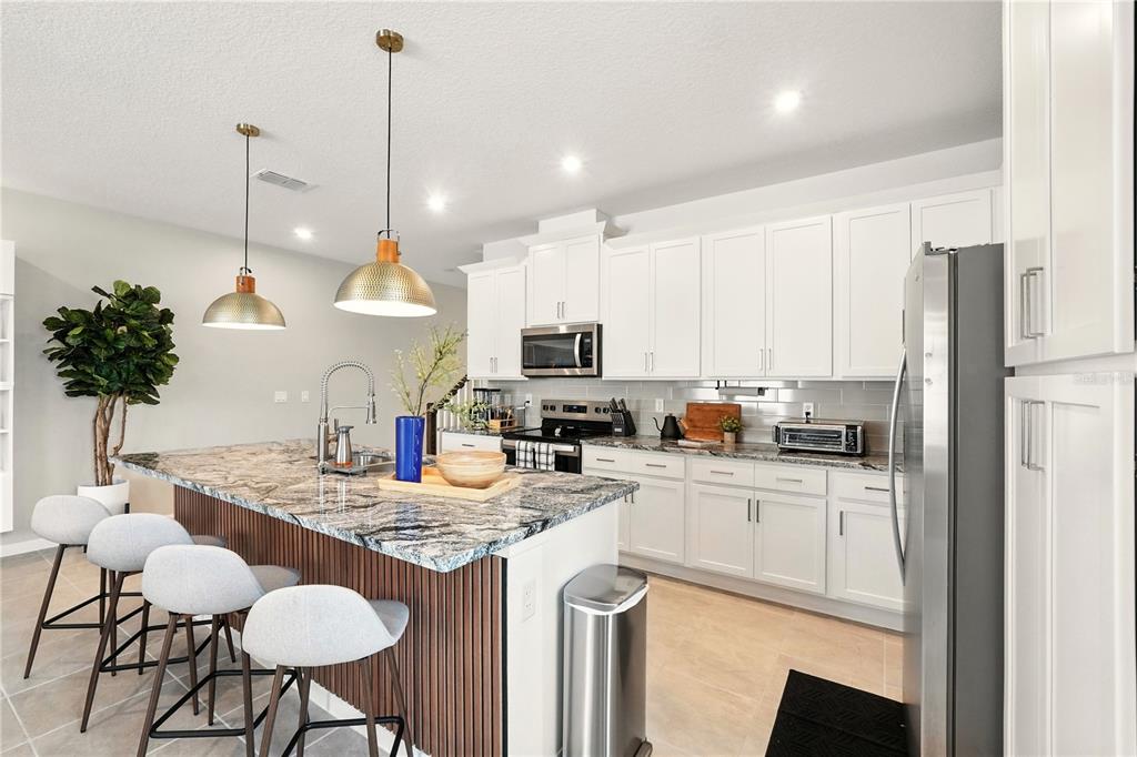 A modern kitchen features white cabinets, a granite island with bar stools, and pendant lighting — 2306 ZABALLINA PLACE, KISSIMMEE, FL