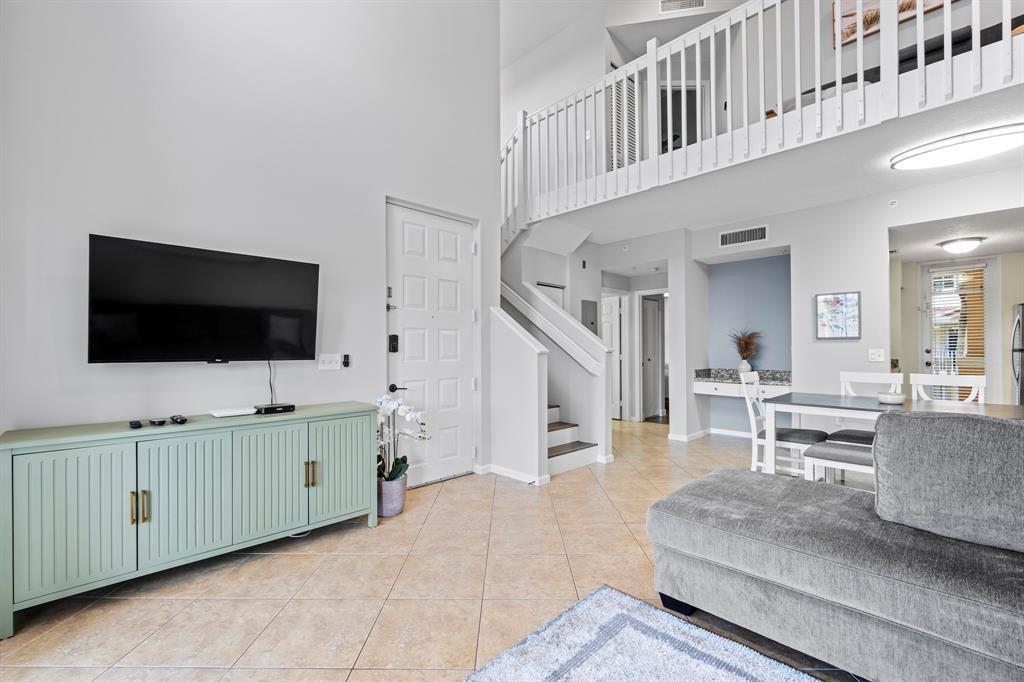A living room features a light green console, a wall-mounted television, and a staircase — 4784 S Central Boulevard # 22, Jupiter FL 33458, JUPITER, FL
