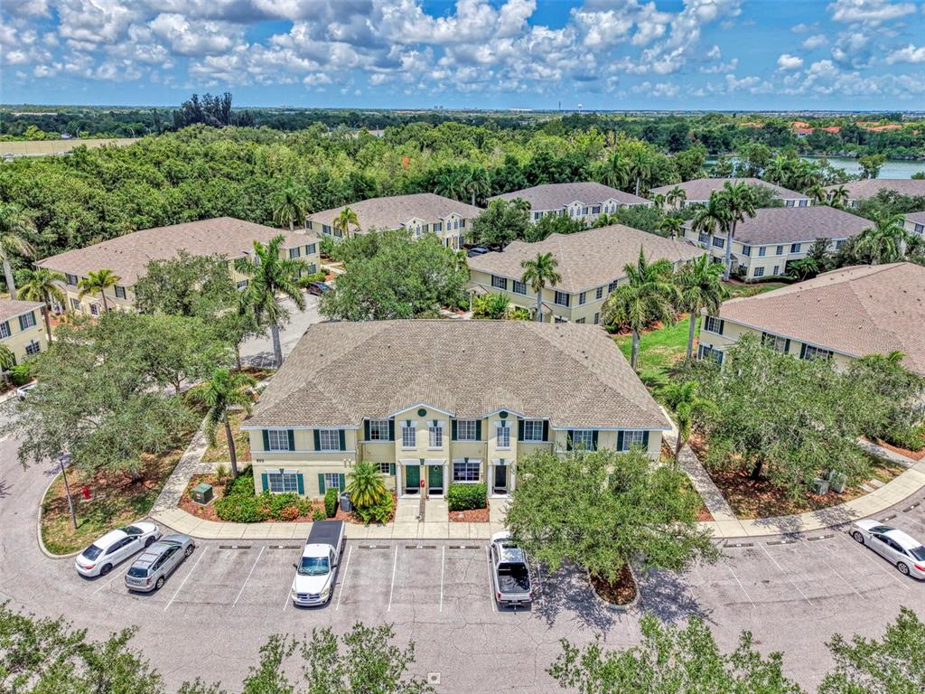 An aerial view shows a multi-story apartment building surrounded by parking lots and lush trees — 305 CAPE HARBOUR LOOP UNIT 104, BRADENTON, FL