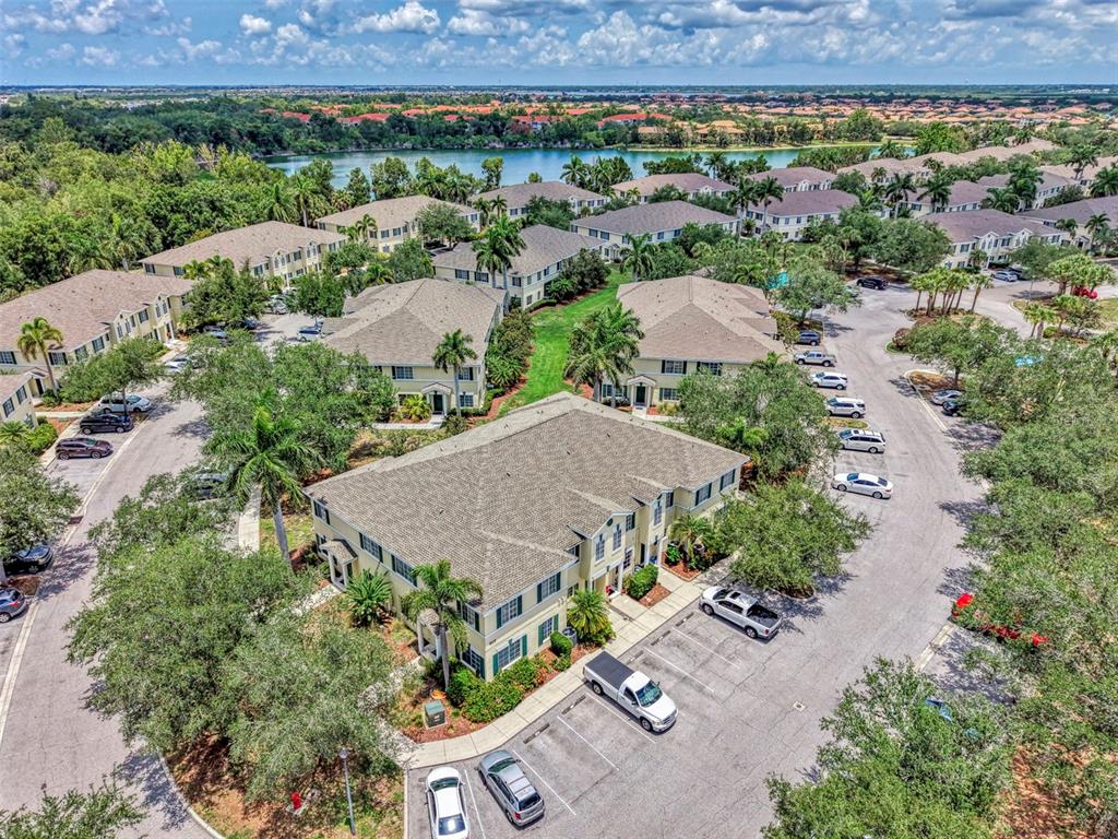An aerial view shows multiple multi-story apartment buildings surrounded by trees, parking lots, and water — 305 CAPE HARBOUR LOOP UNIT 104, BRADENTON, FL