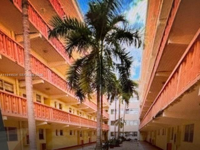 An exterior view of a multi-story apartment complex courtyard featuring a central palm tree — 215 SE 3rd Ave # 307B, Hallandale Beach FL 33009, HALLANDALE BEACH, FL