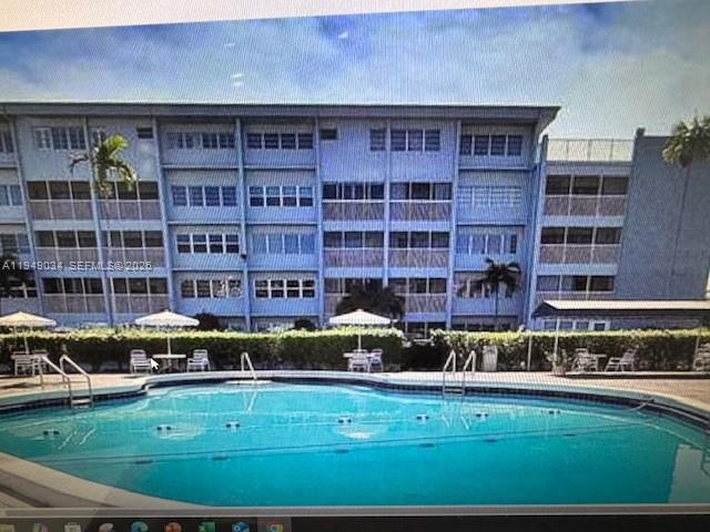 A multi-story apartment building stands behind a swimming pool with lounge chairs and umbrellas — 215 SE 3rd Ave # 307B, Hallandale Beach FL 33009, HALLANDALE BEACH, FL