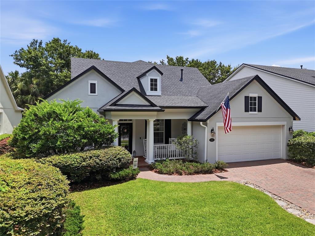 A light-colored house with a brick driveway, a front porch, and an American flag — 103 ASTERBROOKE DRIVE, DELAND, FL