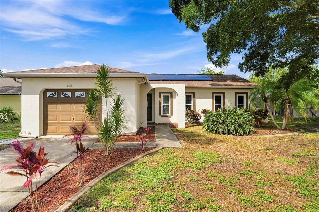 A single-story house with a tan stucco exterior, a one-car garage, and solar panels — 2460 BEACON GROVES BOULEVARD, PALM HARBOR, FL