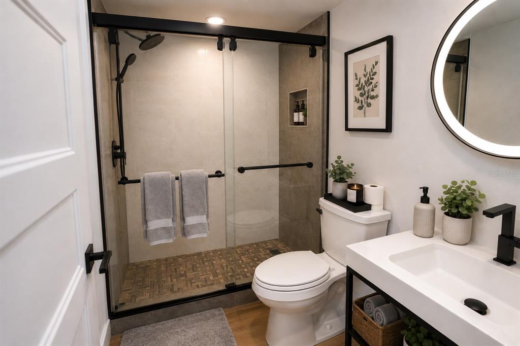A modern bathroom features a glass-enclosed shower, a white vanity, and a round backlit mirror — 4704 CHEVY PLACE UNIT 180, ORLANDO, FL