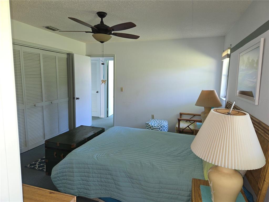 A bedroom features a bed with a blue quilt, a ceiling fan, and louvered closet doors — 2974 CAPTIVA GARDENS DRIVE UNIT 17, SARASOTA, FL