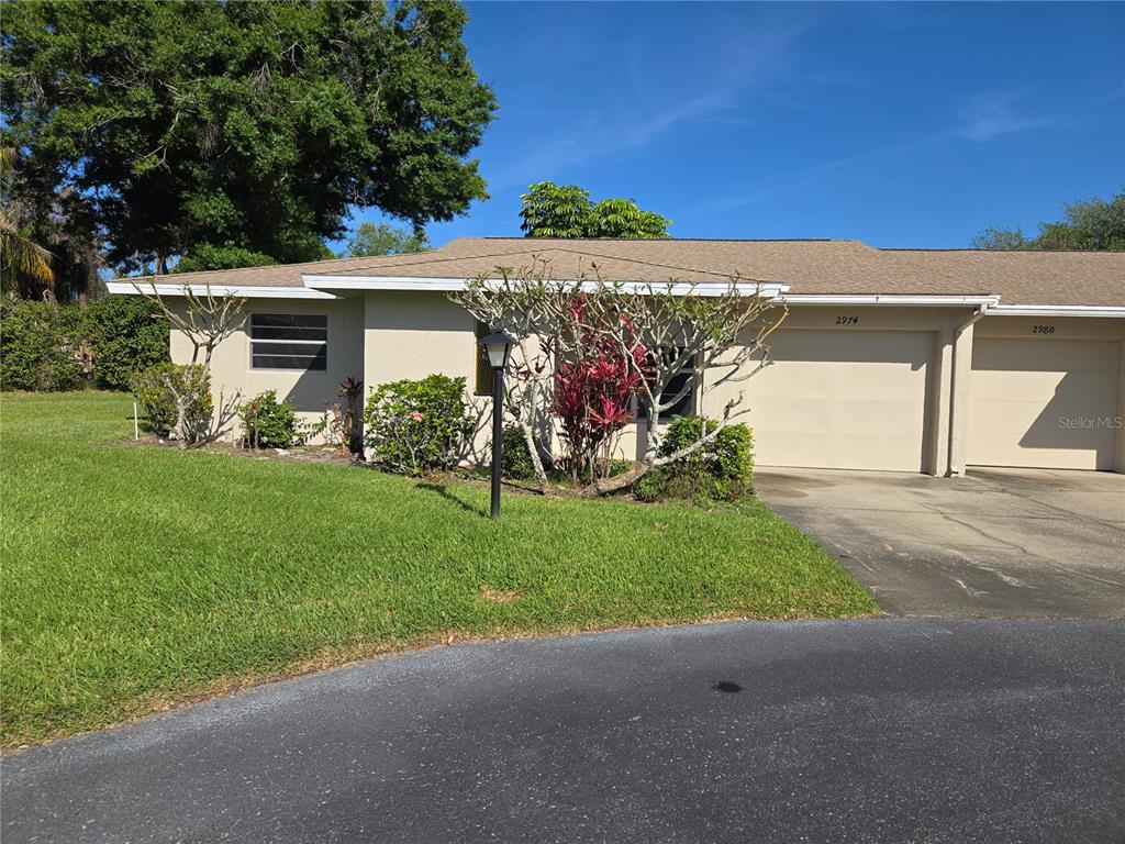 A single-story duplex with beige stucco walls, two garage doors, and a landscaped front yard — 2974 CAPTIVA GARDENS DRIVE UNIT 17, SARASOTA, FL
