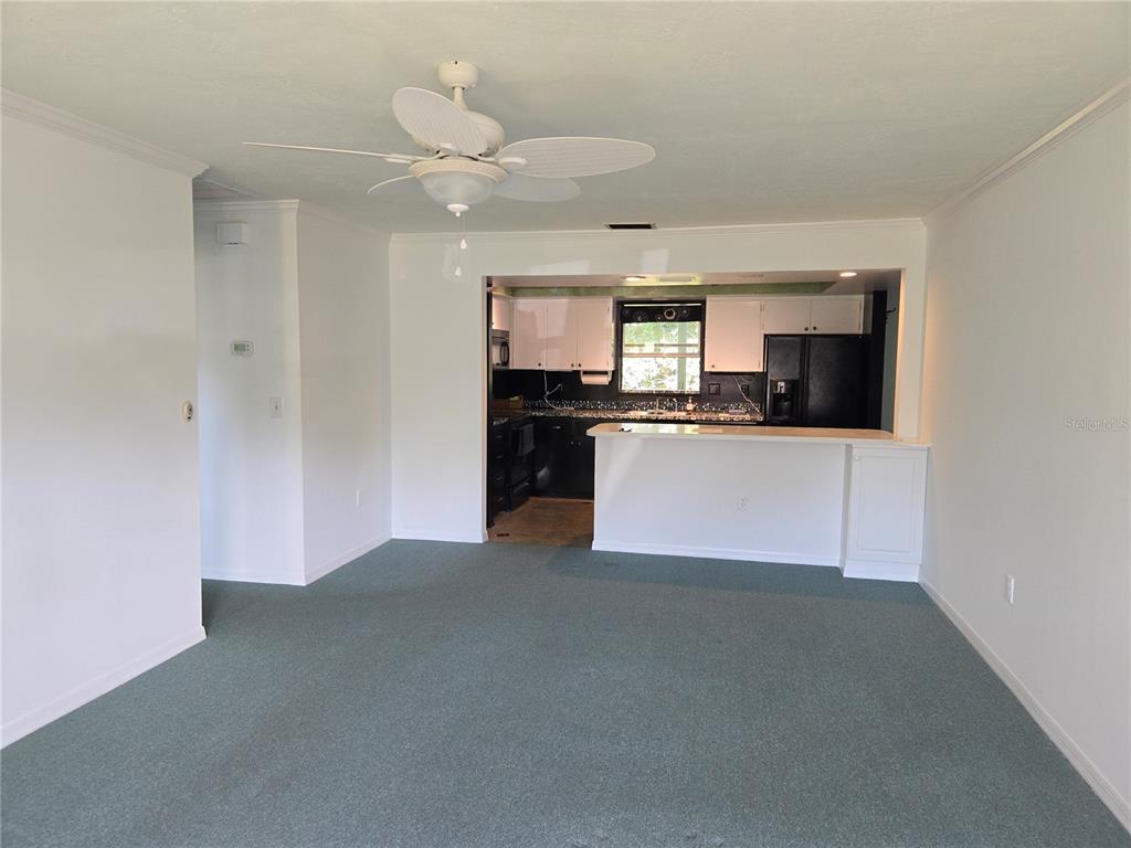 A living room with green carpet and a ceiling fan opens to a kitchen area — 2974 CAPTIVA GARDENS DRIVE UNIT 17, SARASOTA, FL