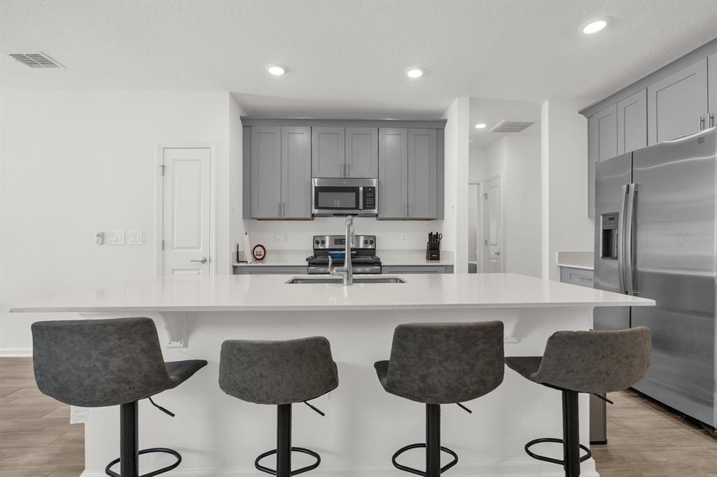 A modern kitchen features a white island with four bar stools and grey upper cabinets — 555 JETT LANE, DAVENPORT, FL
