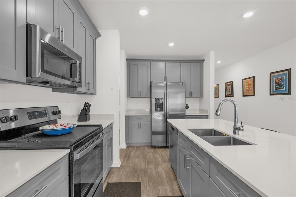 A modern kitchen features gray cabinets, stainless steel appliances, and a white quartz island countertop — 555 JETT LANE, DAVENPORT, FL