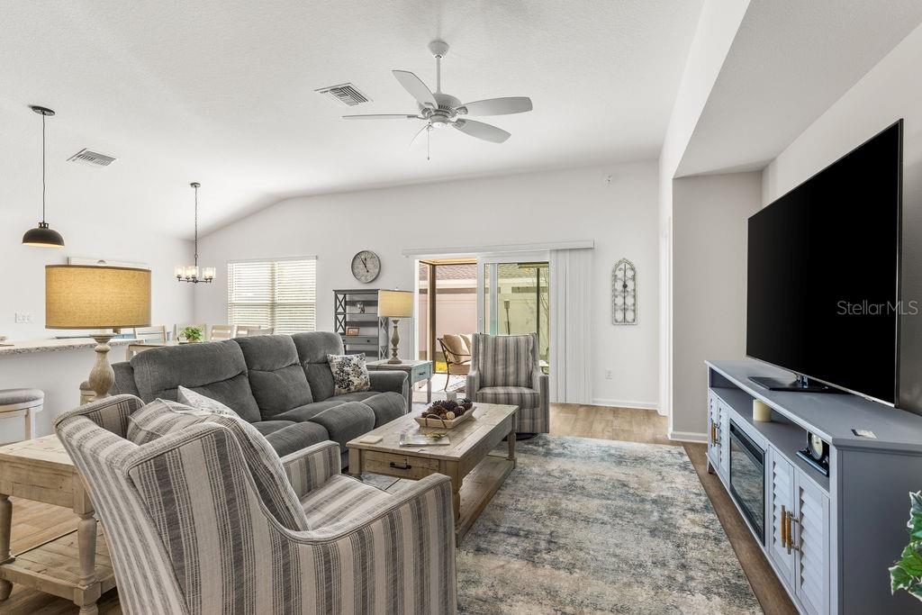 A living room features a gray sofa, striped armchairs, a television, and a ceiling fan — 2938 CHIMBORAZO WAY, THE VILLAGES, FL