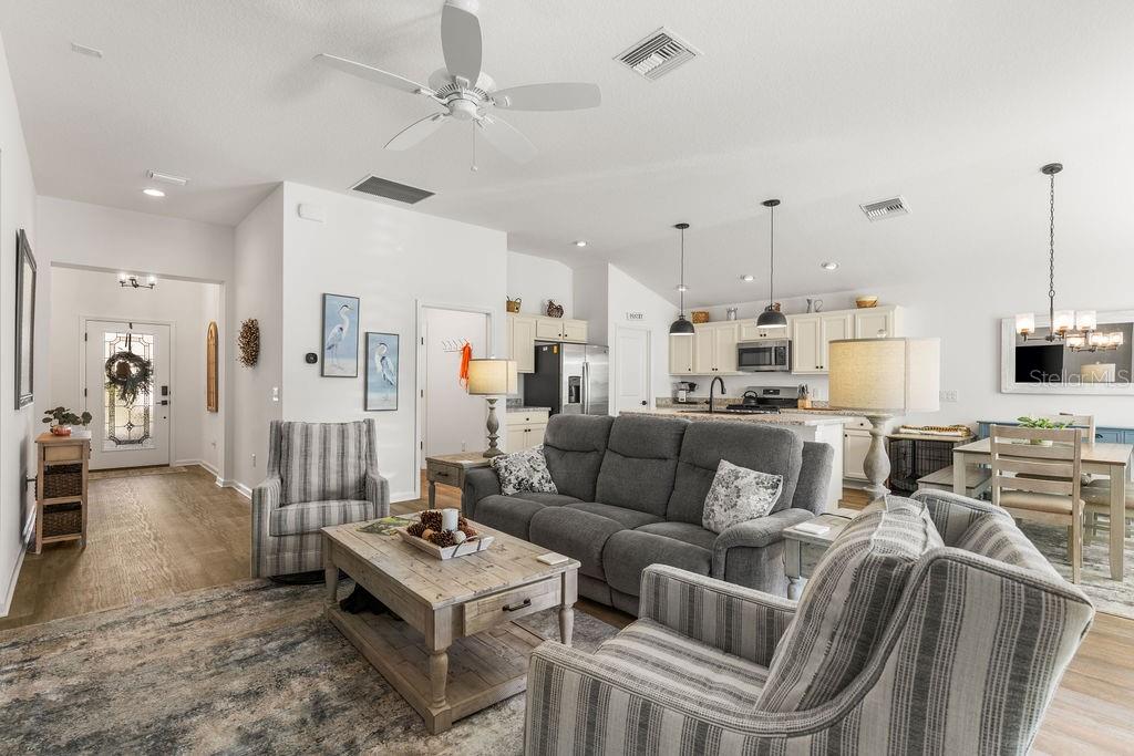 An open-concept living room and kitchen featuring a gray sofa, striped armchairs, and light flooring — 2938 CHIMBORAZO WAY, THE VILLAGES, FL