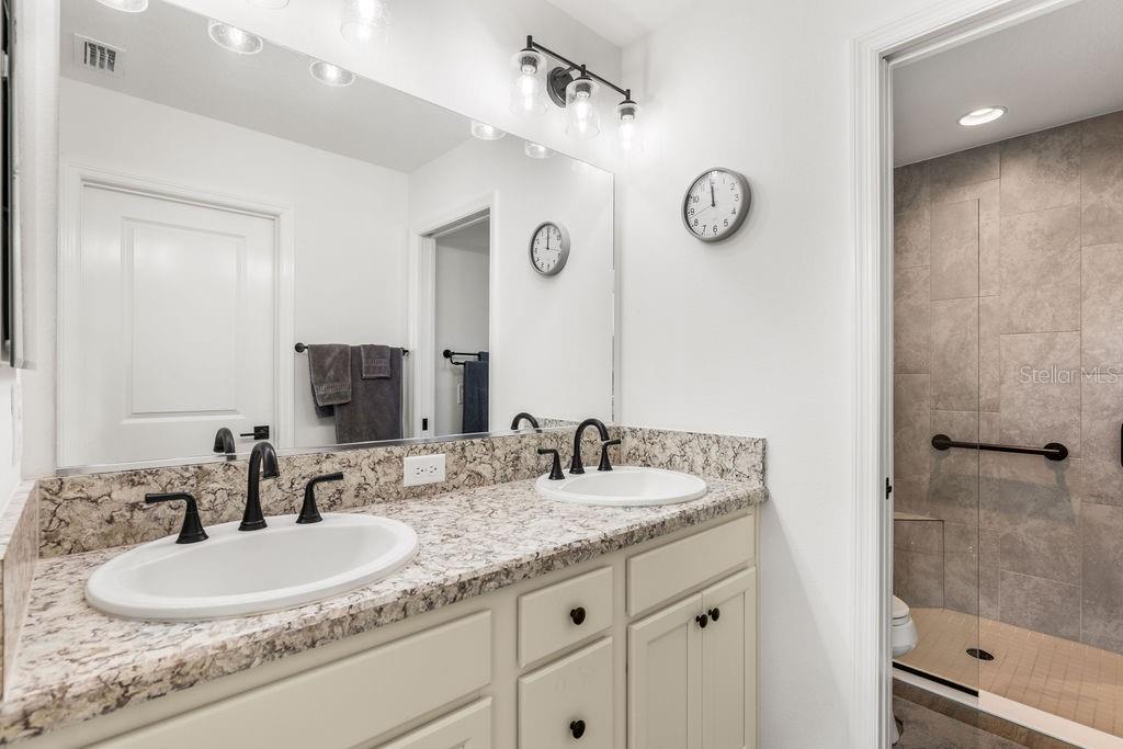 A bathroom features a double vanity with granite countertops, white cabinets, and a walk-in shower — 2938 CHIMBORAZO WAY, THE VILLAGES, FL