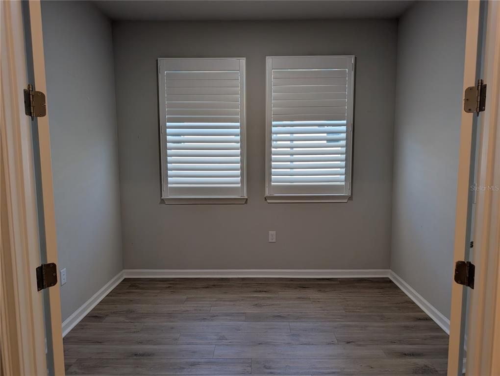 An empty room with gray walls, wood-look flooring, and two windows with white plantation shutters — 3794 MAXWELL PARK DRIVE, SUN CITY CENTER, FL