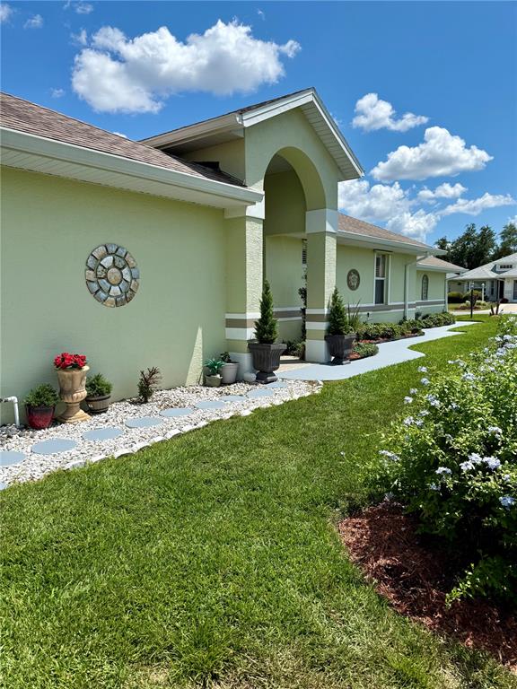 A light green house exterior features a covered entryway, stone wall decor, and landscaping — 21932 ROYAL ST GEORGES LANE, LEESBURG, FL