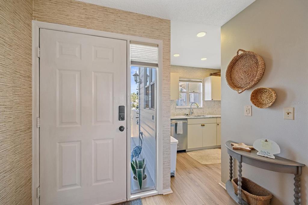 A front entryway with textured wallpaper leads into a kitchen with light-colored cabinets — 851 AUDUBON DRIVE UNIT 851, BRADENTON, FL