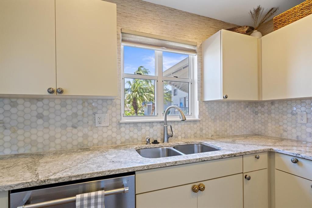 A kitchen features light-colored cabinets, granite countertops, a hexagon tile backsplash, and a stainless sink — 851 AUDUBON DRIVE UNIT 851, BRADENTON, FL