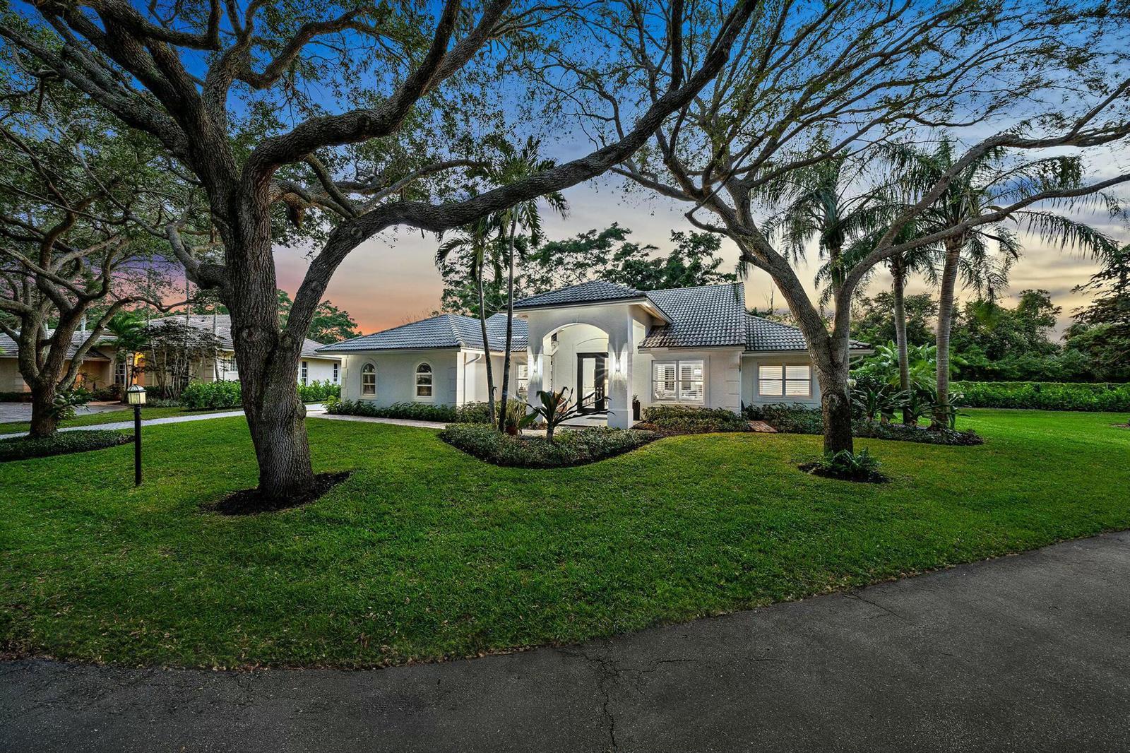 A single-story white house with a tiled roof sits behind a large lawn and trees — 9927 SE Canary Palm Way, Jupiter FL 33469, JUPITER, FL