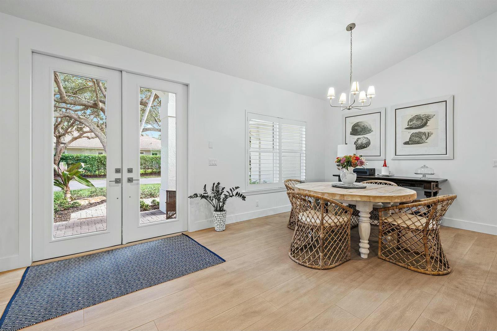 A dining area features a round wooden table, wicker chairs, and double glass doors — 9927 SE Canary Palm Way, Jupiter FL 33469, JUPITER, FL