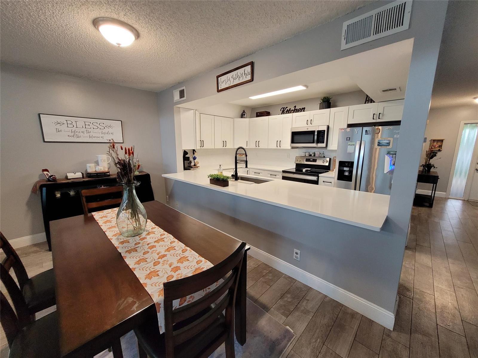 A dining area with a wooden table sits adjacent to an open-concept kitchen with white cabinets — 1146 N University Drive, Plantation FL 33322, PLANTATION, FL
