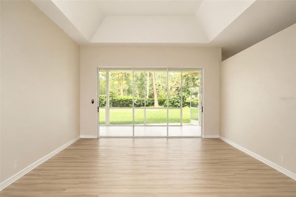 A bright, empty room with light wood-look flooring, a tray ceiling, and large sliding doors — 17316 HIALEAH DRIVE, ODESSA, FL
