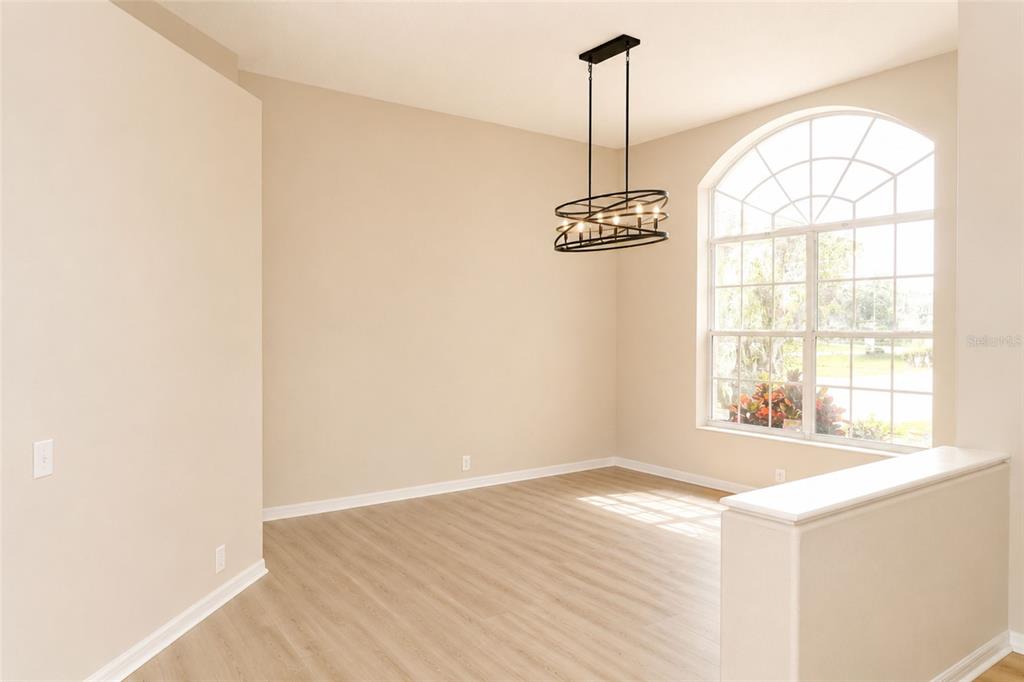 A dining area with light wood-look flooring, a black metal chandelier, and an arched window — 17316 HIALEAH DRIVE, ODESSA, FL