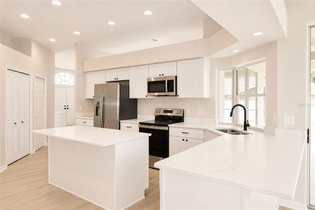 A modern kitchen features white cabinetry, quartz countertops, stainless steel appliances, and a central island — 17316 HIALEAH DRIVE, ODESSA, FL