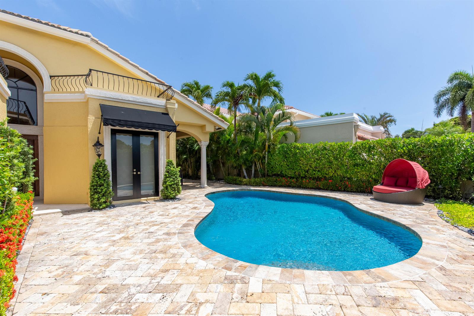 A yellow house with a black awning overlooks a kidney-shaped pool and stone patio — 529 Pelican Way, Delray Beach FL 33483, DELRAY BEACH, FL