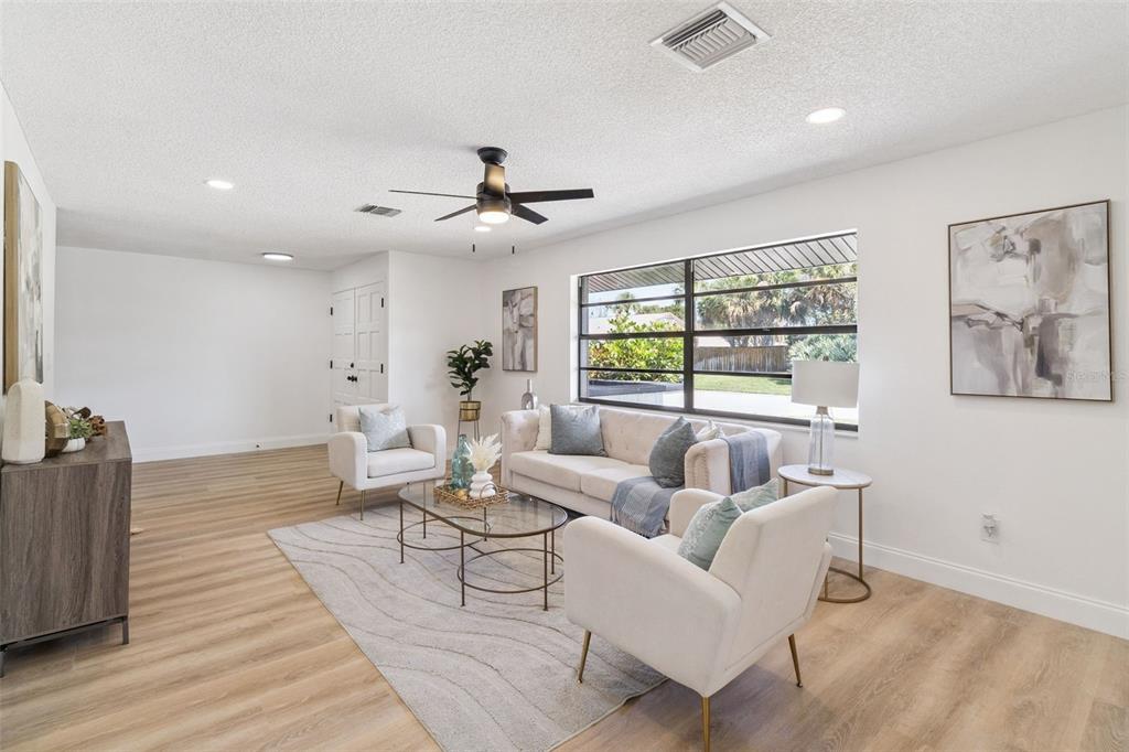 A living room features light wood flooring, a beige sofa, two armchairs, and large windows — 381 E RIVIERA BOULEVARD, INDIALANTIC, FL