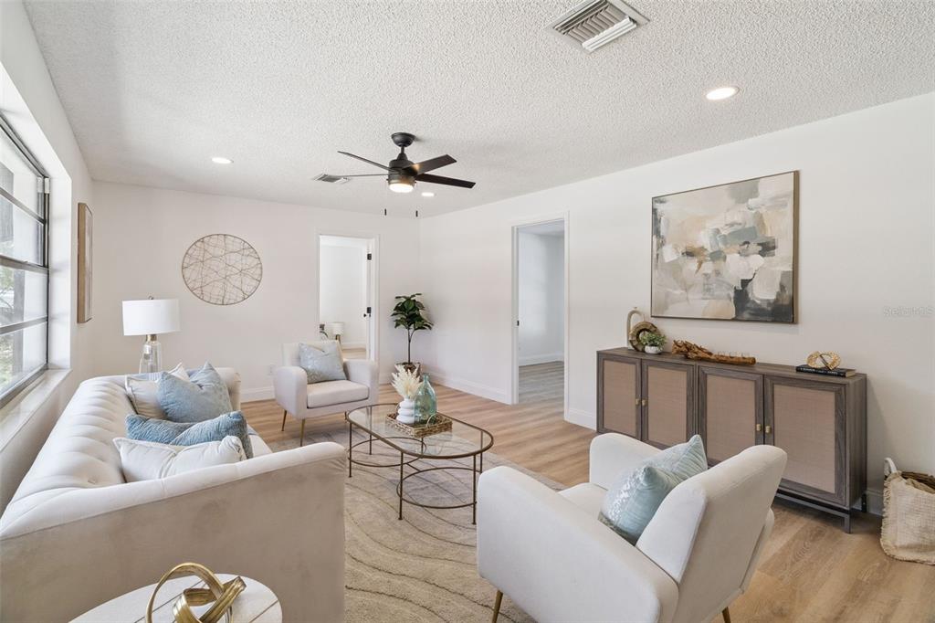 A bright living room features a white sofa, two armchairs, a glass coffee table, and cabinetry — 381 E RIVIERA BOULEVARD, INDIALANTIC, FL