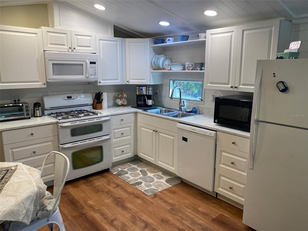 A kitchen features white cabinets, stainless steel appliances, wood-look flooring, and an open shelf display — 1300 N RIVER ROAD UNIT W 86, VENICE, FL